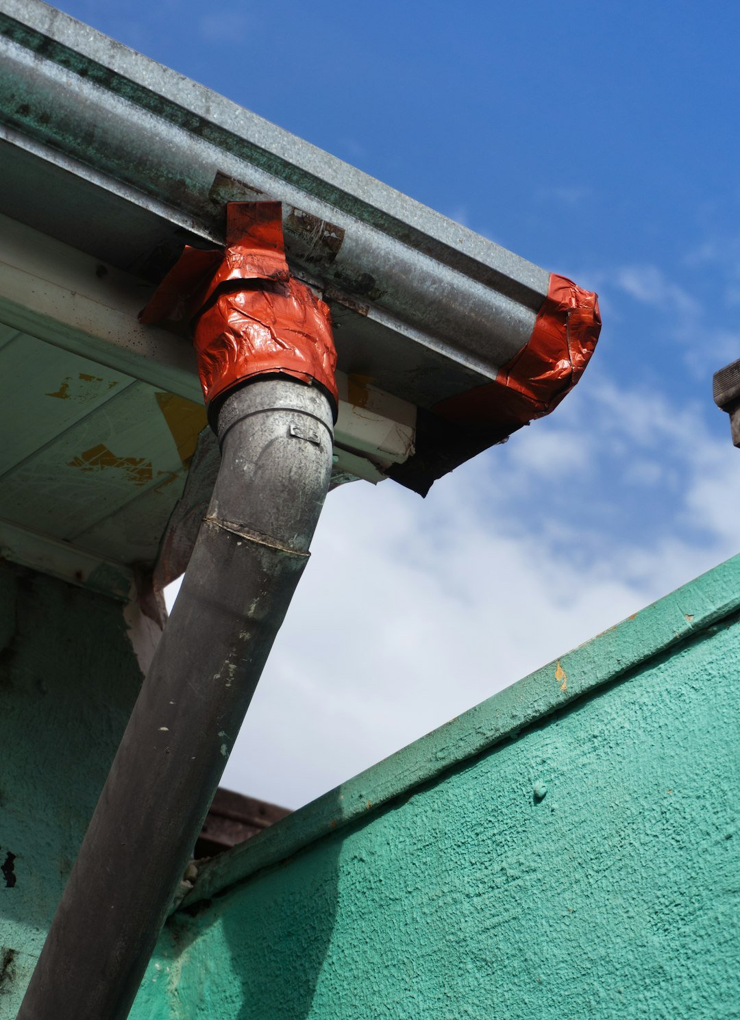 gallery-09 A rusted drainpipe held together with orange tape on a weathered teal wall. The colors of improvisation.